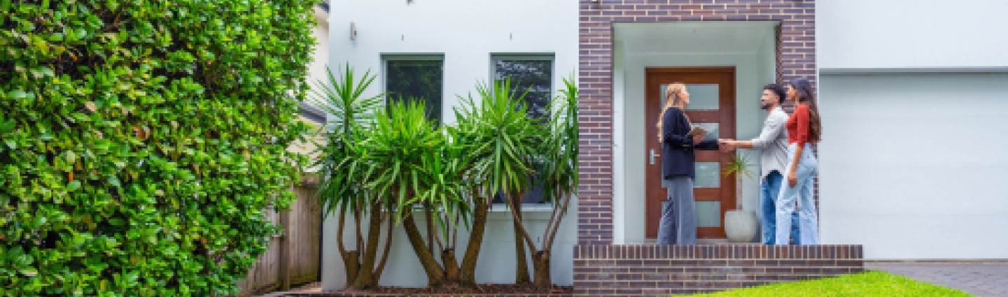 Couple meeting with a property agent outside a new home, discussing investment opportunities.
